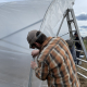 person putting cover on high tunnel frame