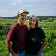 two people pose outdoors in front of farmland