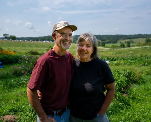 two people pose outdoors in front of farmland