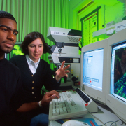 two people seated, looking at a computer display screen
